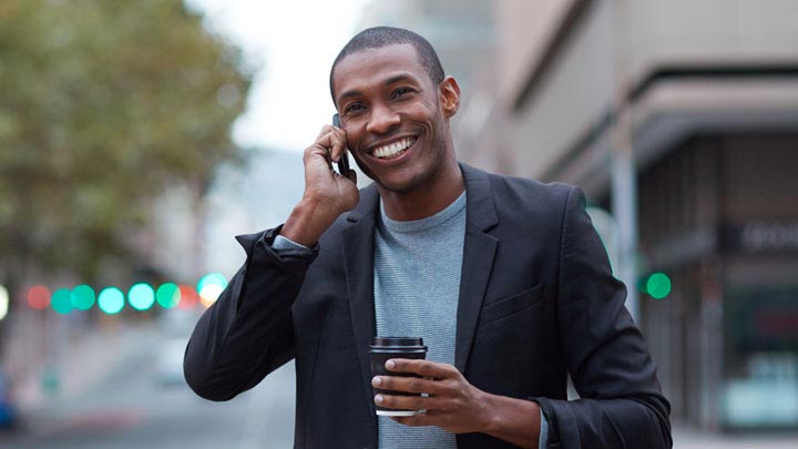 Mann som smiler til telefonen mens han går på gaten