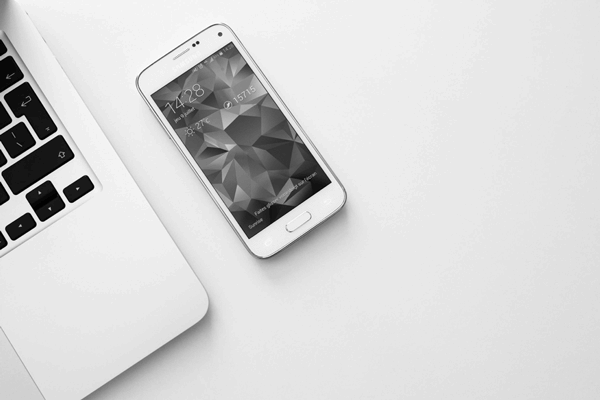 Part of a laptop and cellphone laying on a white desk